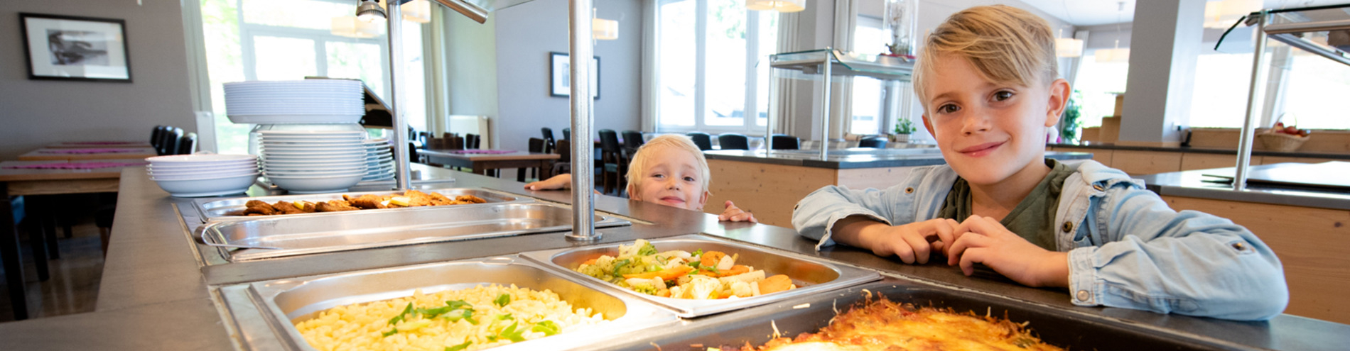 Zwei Jungen schauen aufs Buffet mit verschiedenen warmen Gerichten im Restaurant. 