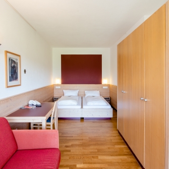 Junior-Appartement mit zwei Doppelbett, rotem Sofa, Holzboden, großem Kleiderschrank und Schreibtisch mit Telefon.