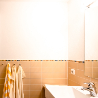 Badezimmer vom Familien-Appartement mit beigen Fliesen, einer Dusche mit Glastür, Handtüchern an Haken und einem Waschbecken mit Spiegel.